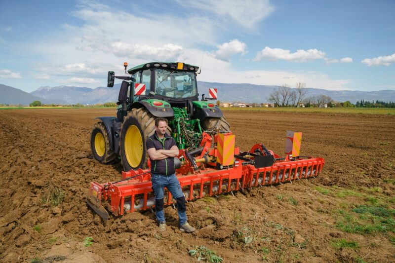 A skilled farmer proudly stands next to his plowing tractor, demonstrating his expertise in field