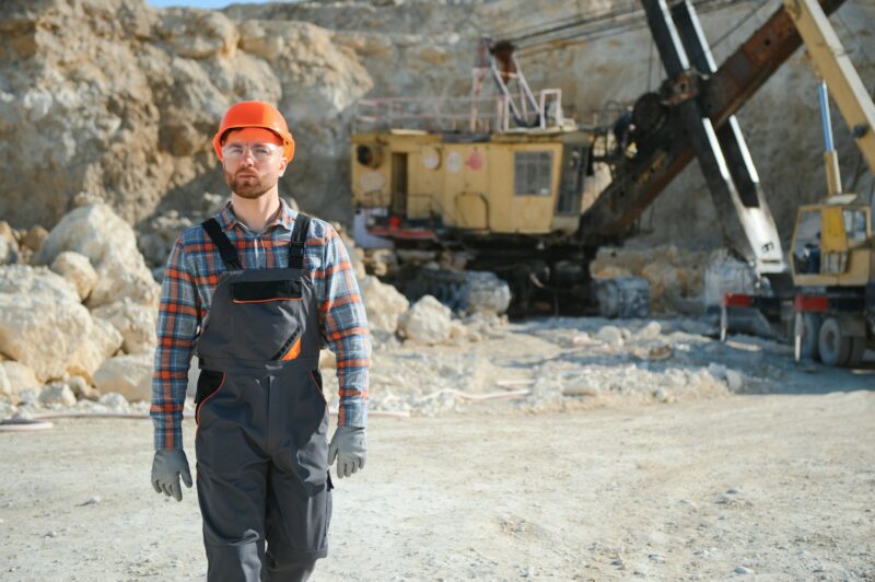 A worker in a helmet stands on the background of an excavator in a quarry