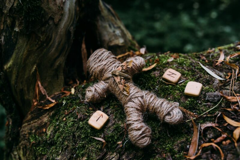 A woven voodoo doll of threads, a moth and runes in a ritual in a mysterious forest.