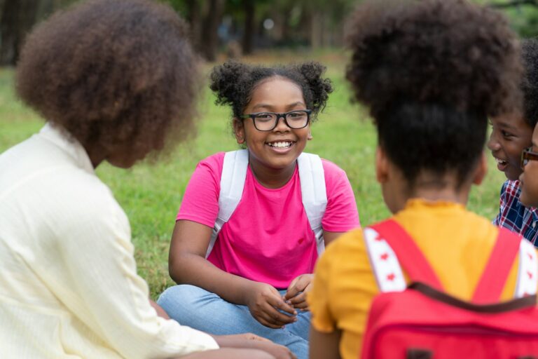 African American girl with backpacks and children sitting on the grass in the park