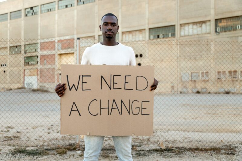 African American man looking at camera hold we need a change banner protesting. Copy space.