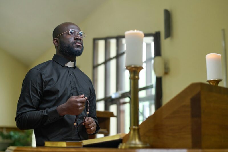 African American priest in black casualwear holding rosary beads during pray