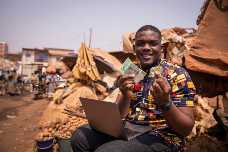 African boy at the market holding FCFA francs and a Bitcoin coin, cryptocurrencies in africa