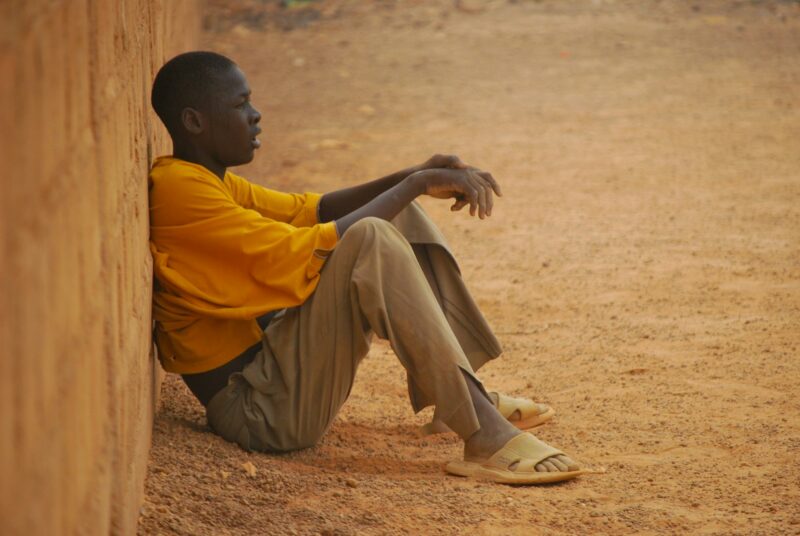 African boy sitting against the wall looking at a soccer game