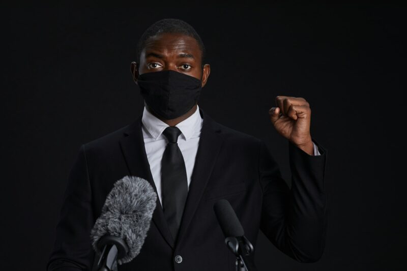 African Man Speaking to Microphone Wearing Mask