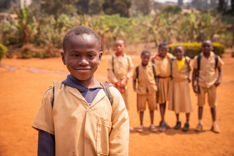 African schoolboy with Down syndrome in the schoolyard with his school mates in the background.