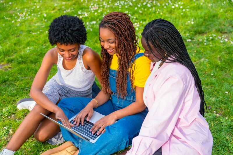 African students using laptop together sitting on a park