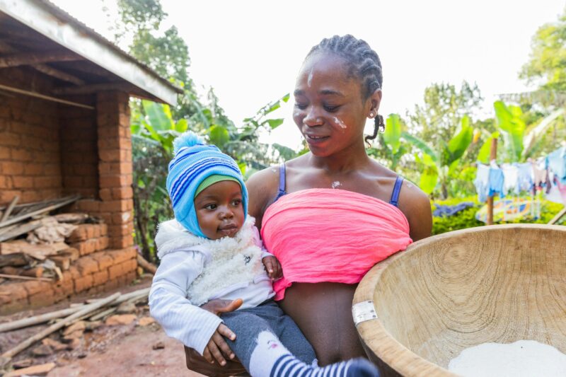 An African mother holds her newborn son and a basket with flour for cooking