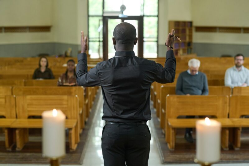 Back of African American priest in black shirt and pants blessing parishioners