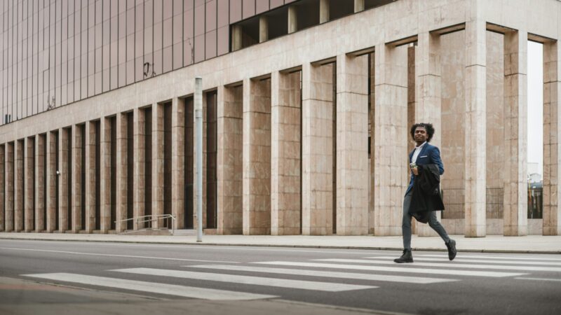 Big long shot of young african businessman crossing the street with happiness, space for copy