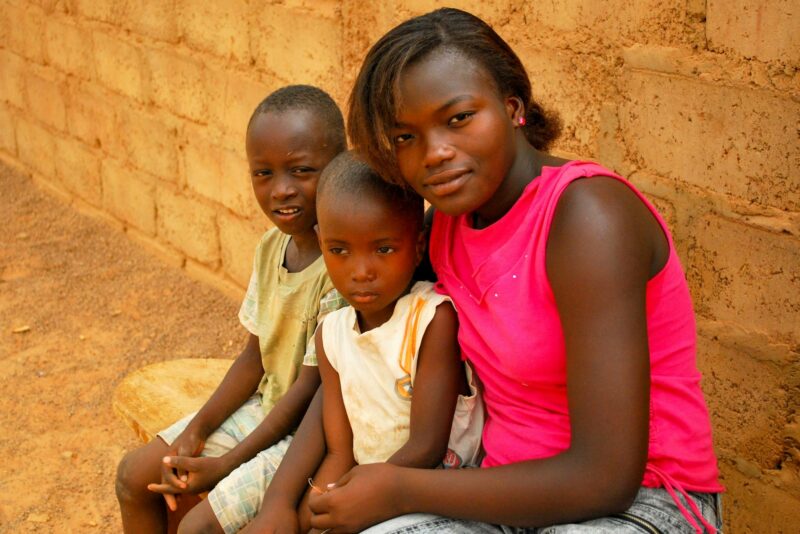 Black African teenage girl sitting outside on a bench with her little brothers
