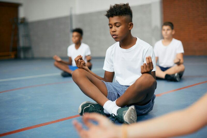 Black elementary student doing breathing exercise while practicing Yoga on physical education class.