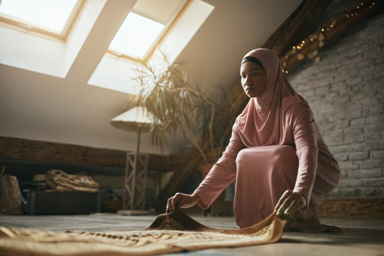 Black Muslim woman placing prayer mat on the floor at home.