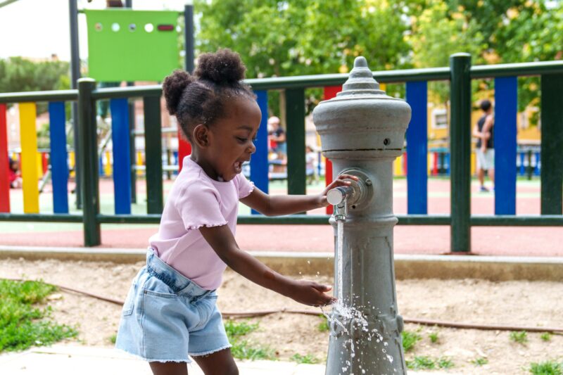 Bubbling Joy: African girl gleefully playing with water in city park fountain.