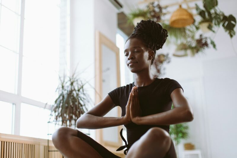 Calm and spiritual young interracial woman with hands together in namaste in lotus asana posture