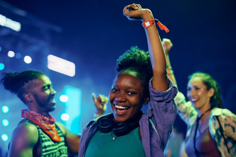 Cheerful black woman dancing during summer music festival and looking at camera.