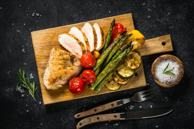Chicken breast grilled with vegetables on black table.