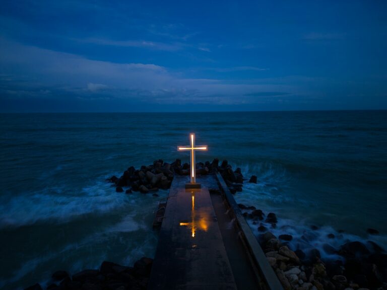 christian cross standing on pier in the sea or ocean with dramatic sky at night