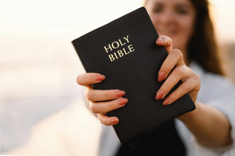 Christian woman holds bible in her hands. Reading the Holy Bible on the sea during beautiful sunset