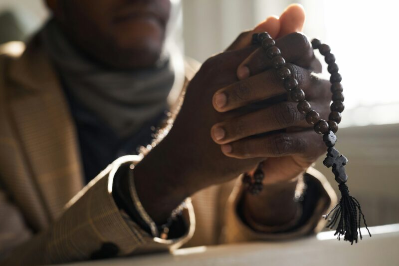 Close Up of Black Man Praying in Church Hands Holding Rosary