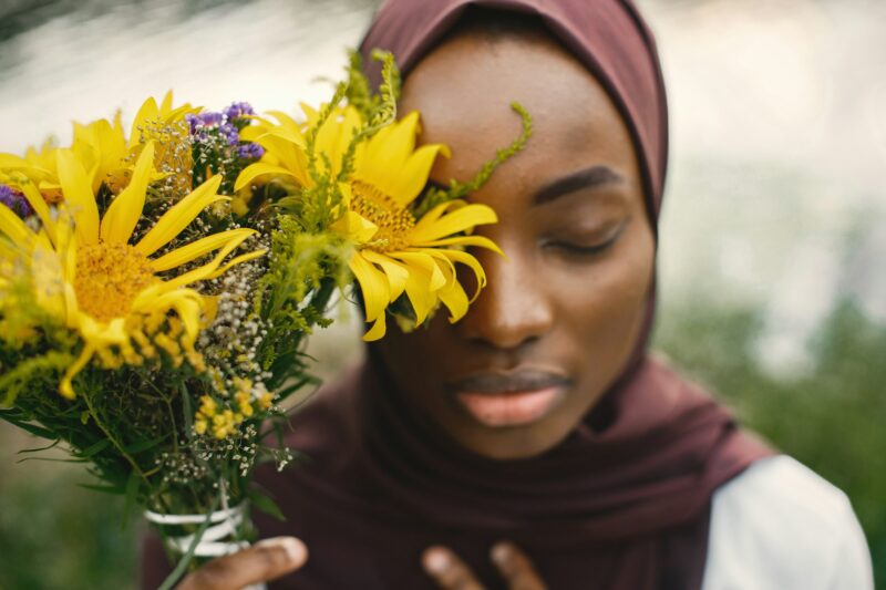 Close up portrait of muslim woman covering half of face with a yellow flowers