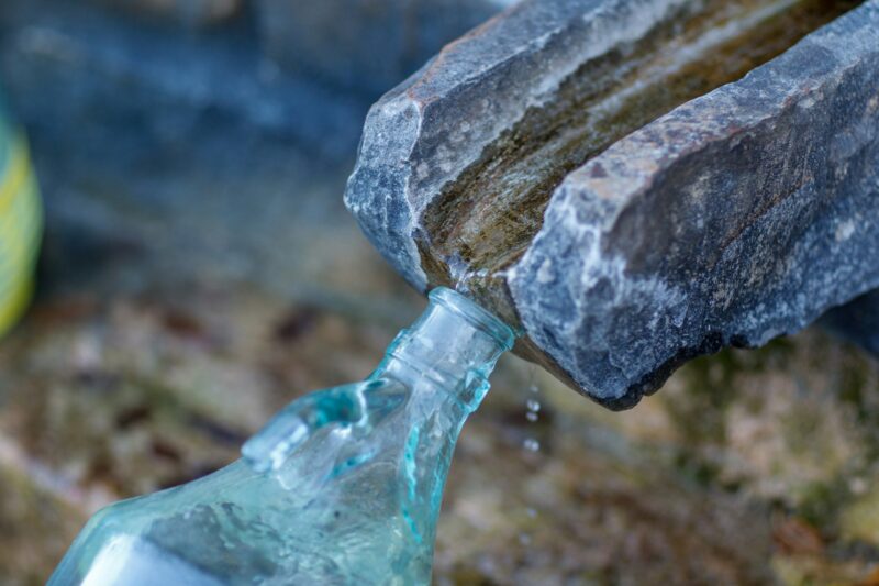 collecting safe spring mineral water from source in mountain for human consumption with glass bottle