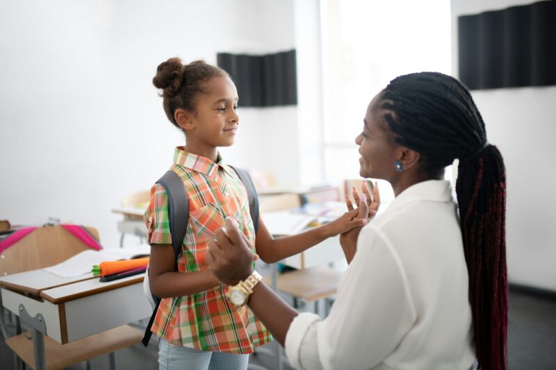 Dark-skinned teacher supporting little African-American girl