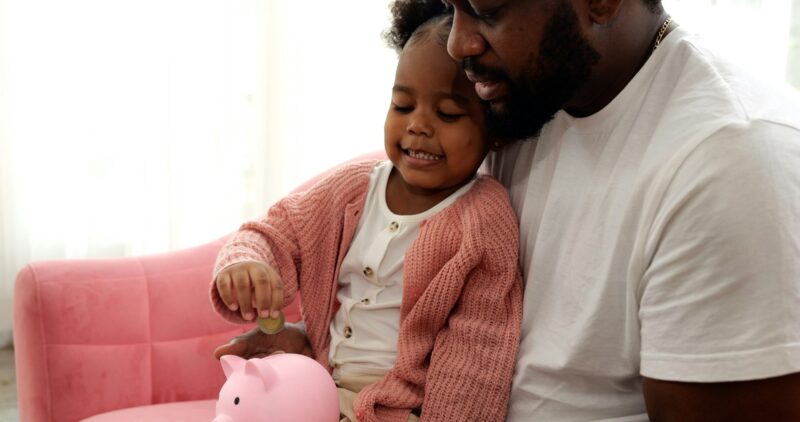 Daughter and father saving money putting coin of cash into ceramic piggy bank