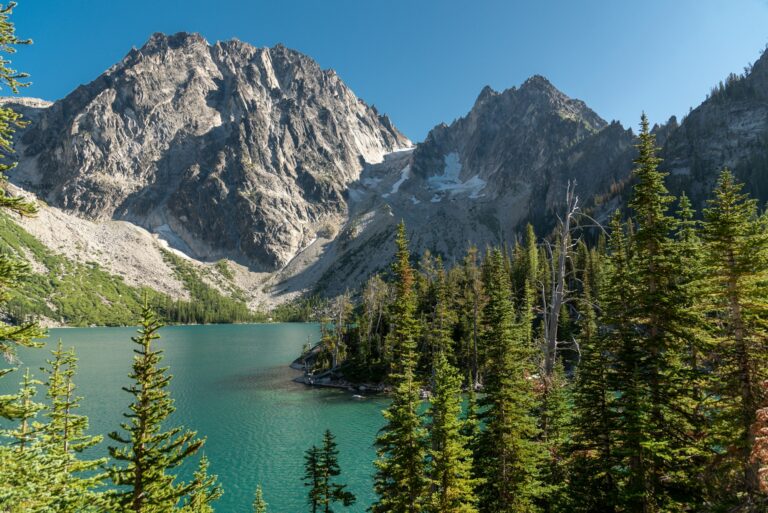 Dramatic landscape alpine lake in evergreen forest surrounded by jagged mountain peaks.