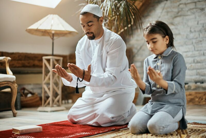 Father and daughter of Islamic faith praying together at home.
