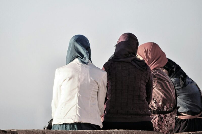 Group of women with colorful hijabs sitting on a bench and talking under a grey sky