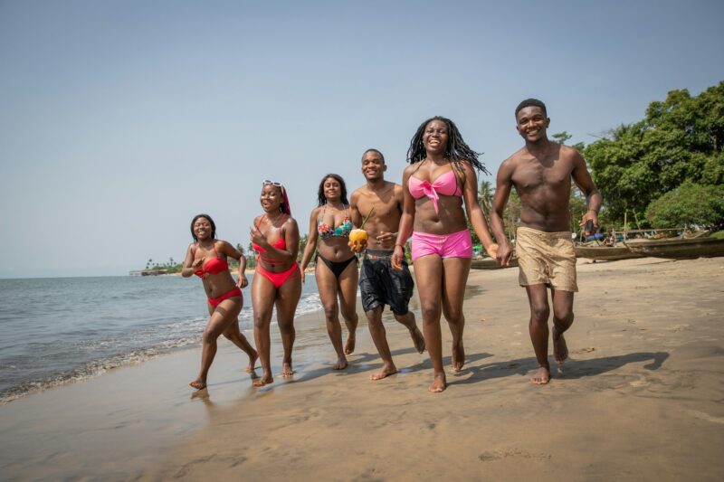 Group of young African friends, males and females, having fun on a tropical beach, carefree life