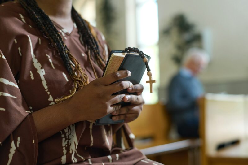 Hands of young black woman with Holy Bible and rosary beads with cross
