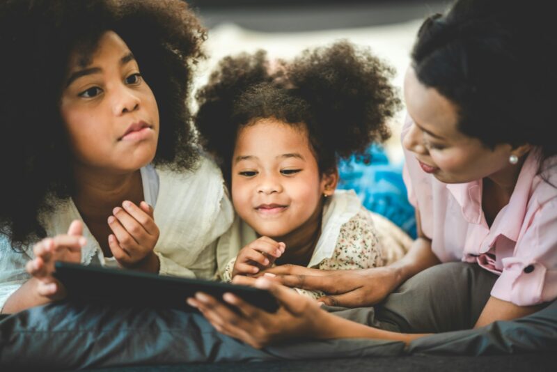 Happy American African family watching tablet on bed at home