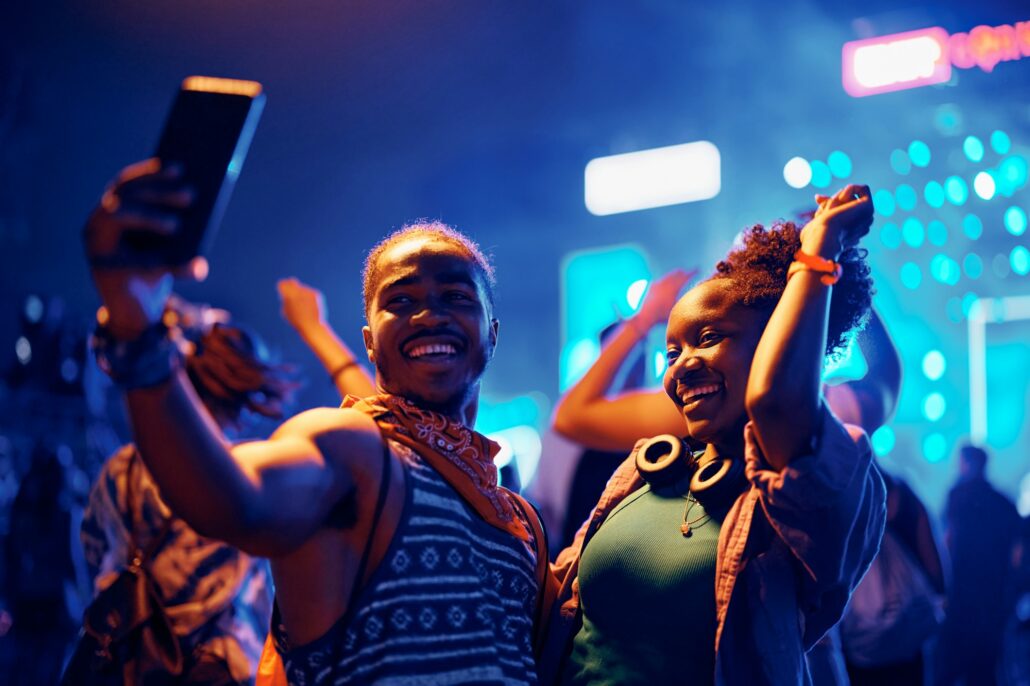 Happy black couple taking selfie while dancing at open air music concert at night.