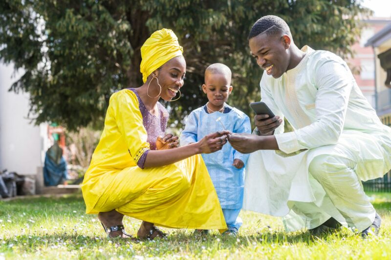 happy family with toddler picking flower holding smartphone