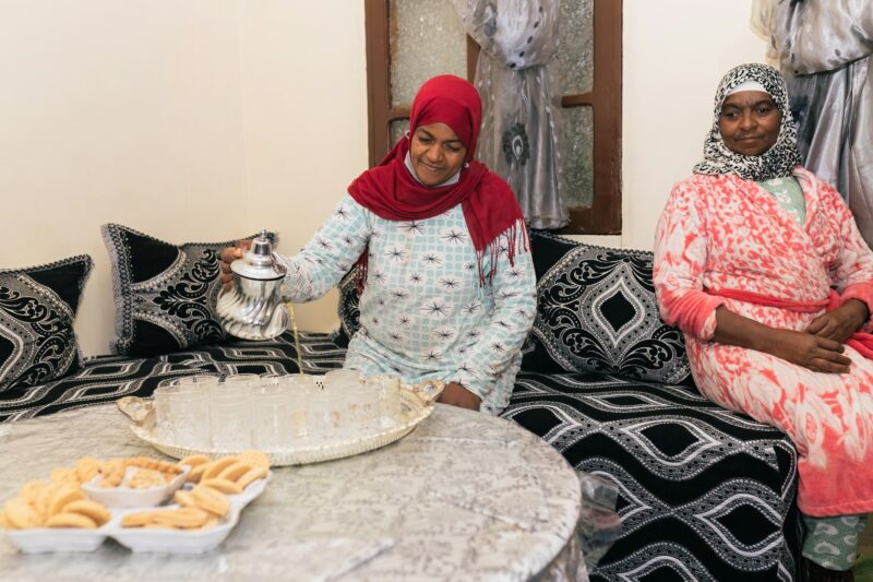 Happy Muslim women in hijab sitting on cozy chair and serving tea