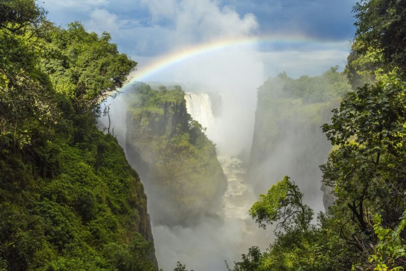 High angle view of waterfall cascading down overgrown rocks, single rainbow.