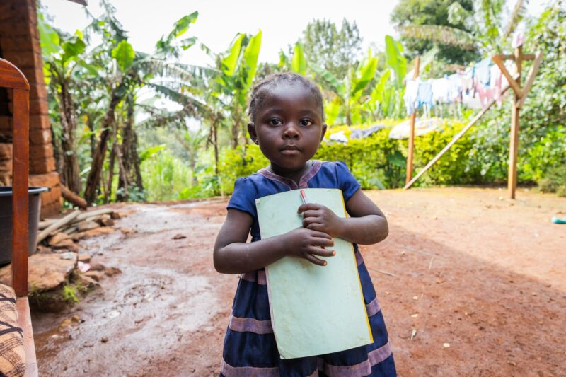 Little shy baby girl holding a notebook and a pen in her arms outdoor in the village