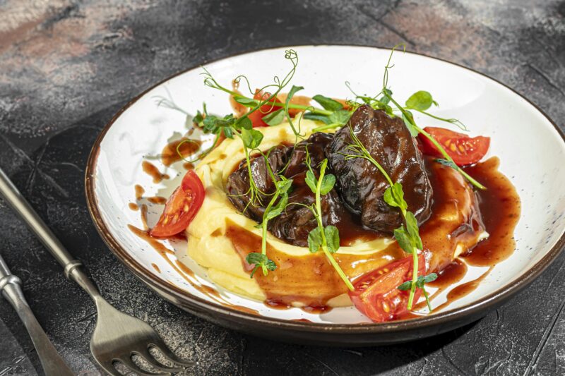 Mashed potatoes with beef in sweet and sour sauce, decorated with tomatoes and microgreens.