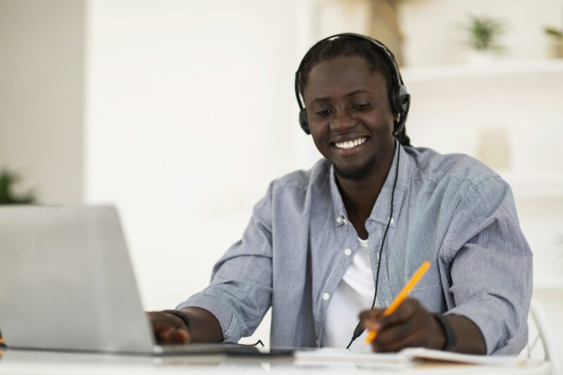 Online Education. Smiling Black Man In Headset Study With Laptop At Home