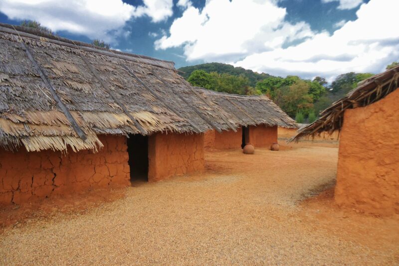 Orange clay huts with thatched roofs of west African village, exhibit recreation