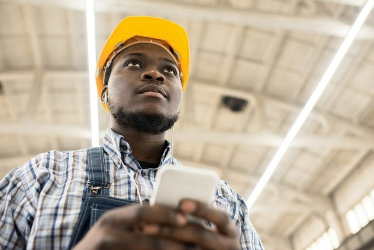 Pensive engineer texting sms at construction site