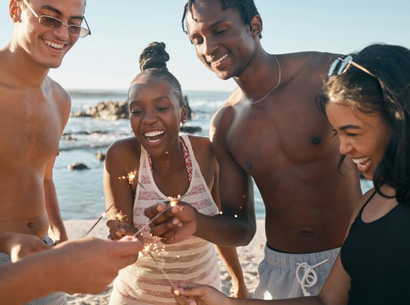 People, laughing and sparkler in beach celebration, party event or birthday social gathering. Firew