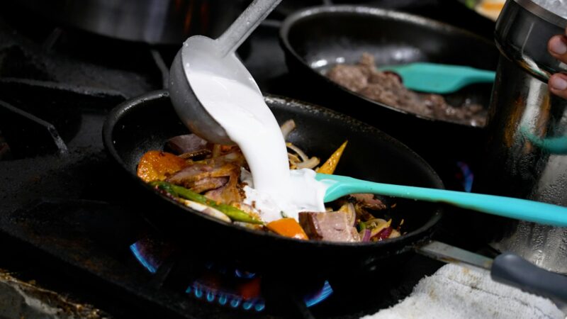 Person cooking and preparing traditional Thai cuisine in pans.