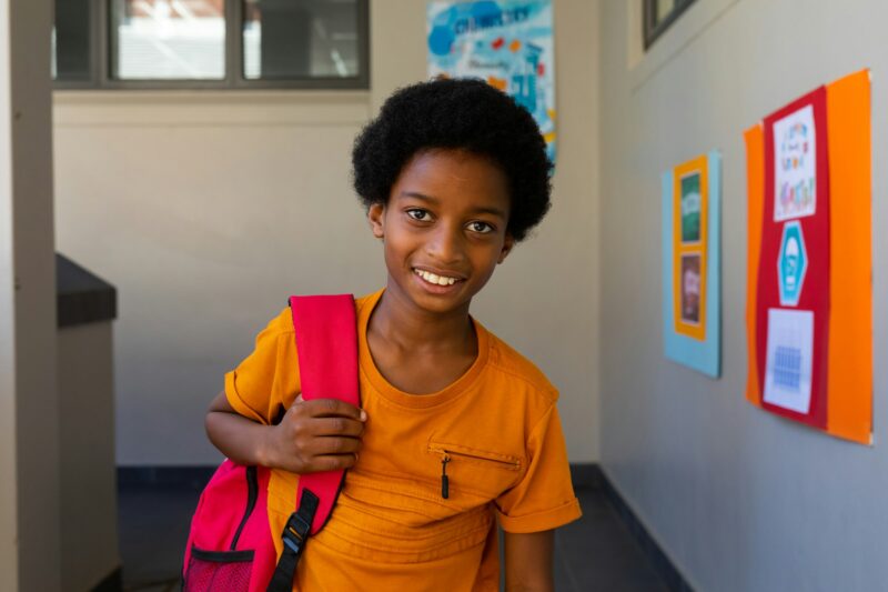 Portrait of happy biracial schoolboy with school bag at school