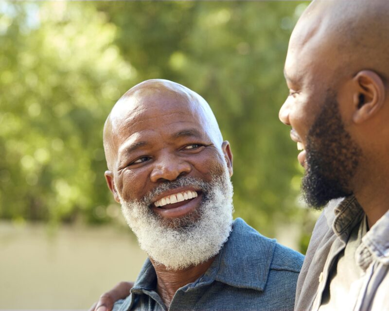 Portrait Of Loving Senior Father With Adult Son Standing Outdoors In Garden Park Or Countryside