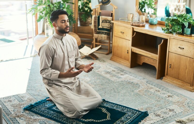 Shot of a young muslim man praying in the lounge at home