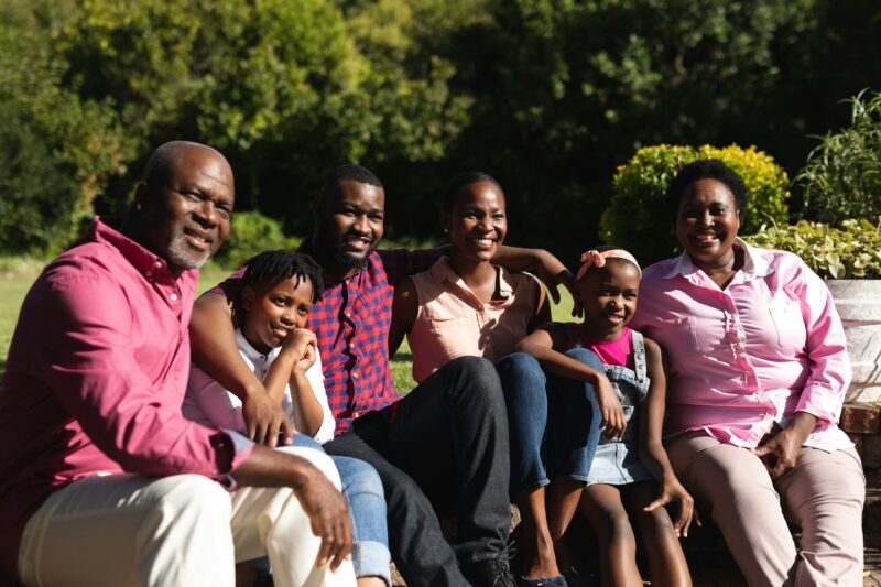 Smiling african american parents with children and their grandparents sitting embracing outdoors