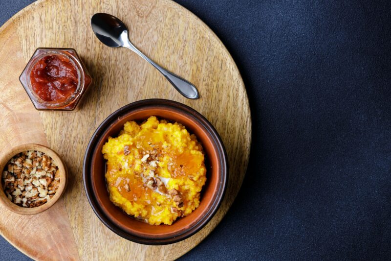 Sweet pumpkin porridge in clay bowl with jam and nuts
